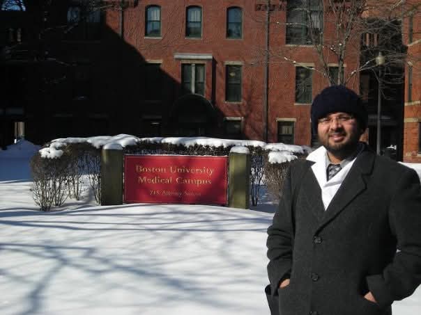 Dr. M. Khawar Nazir, standing in front of Boston University Medical Campus during his training, wearing a grey coat and a blue hat against a snowy backdrop.