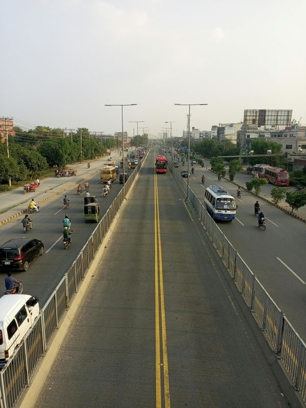 A busy road in Lahore, Pakistan, with public transport, motorcycles, and cars. The city's urban environment exposes residents to dust, smoke, and smog, which can trigger eczema flare-ups and other skin concerns. Wearing a mask on high-smog days and using air purifiers indoors can help protect skin health.